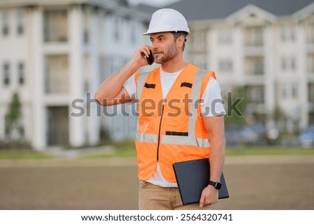 Builder using phone. Portrait of builder in a construction site. Builder ready to build new house. Construction builder wear building uniform and helmet.