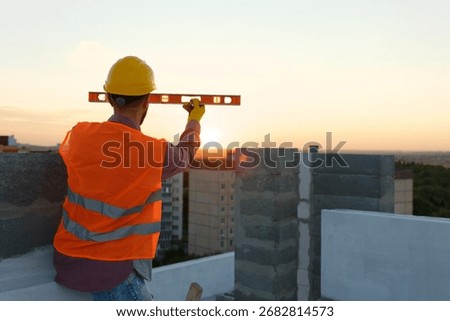 Builder using spirit level at construction site with crane in background, ensuring accurate measurements for building project