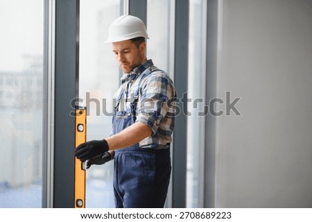 Builder using spirit level ensuring precise vertical alignment during window installation in building under construction