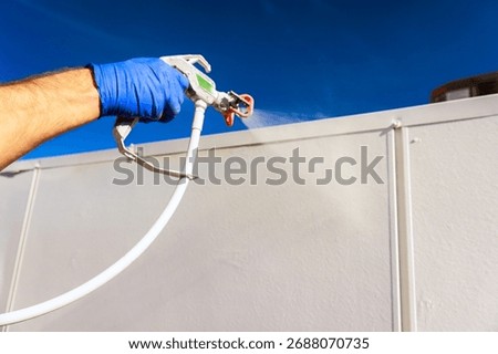 Builder is using spray gun to apply paint on wall in during construction activity.