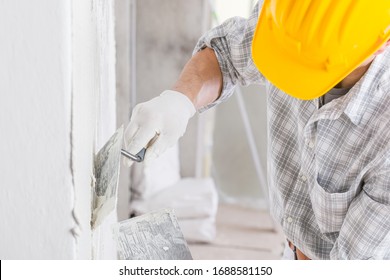 Builder using a trowel to add plaster to a white wall during repairs for a damp area caused by water leakage or moisture