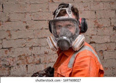 Builder Wearing Full Face Respirator Mask And Ear Defenders For Working In Dusty And Noisy Environment. 