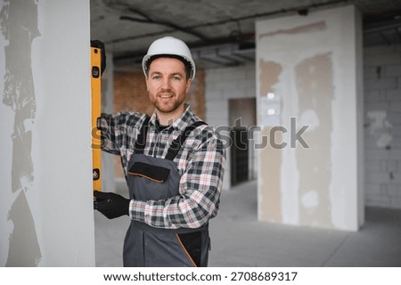 Builder wearing uniform and hardhat using spirit level during house renovation checks vertical alignment of wall
