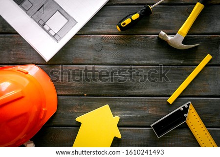 Builder work desk with hard hat, instruments and blueprints on dark wooden background top-down frame copy space