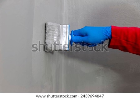A builder worker applying waterproofing paint to the bathroom wall and floor. Applying waterproofing in the bathroom.