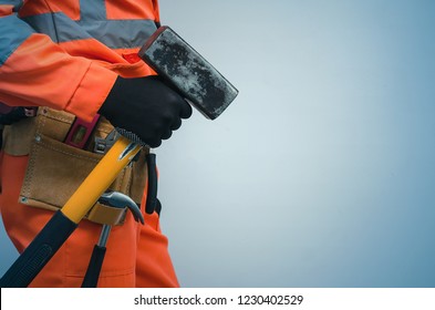 Builder Worker Holding In Hands A Big Sledgehammer Isolated On Blue Background. Under Construction Concept.