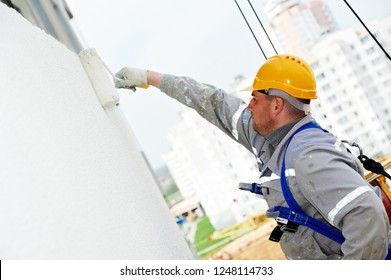 builder worker painting facade of building with roller