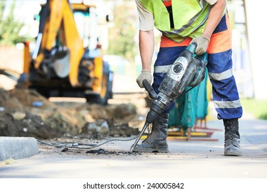 Builder worker and pneumatic hammer drill equipment breaking asphalt at road construction site