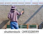Builder worker using trowel to plastering cement on the wall inside of house construction site, rear view with copy space
