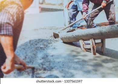 Builder Workers Spreading Concrete Mix With  Hoe While  Truck Mounted Concrete Pump Pouring Cement On Foundation At House Construction Site In Sunny Day.