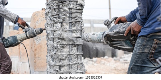 Builder workers using pneumatic hammer drill equipment breaking concrete bridge pillars at road construction site.