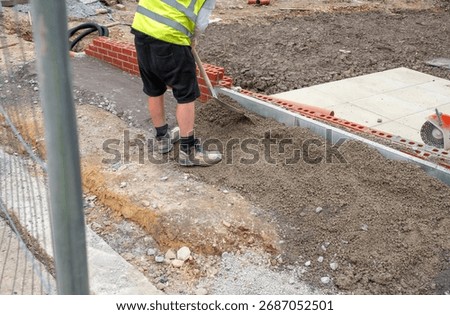 Builder working on sidewalk installation using shovel to place concrete around new edging pin kerb
