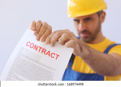 Builder or workman in a safety helmet ripping up a contract which he is holding extended in front of him with focus to the document