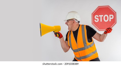 Builder yells at the megaphone. Person emotionally warns of danger. Stop sign in man hands. Man with a stop sign. Portrait of excited man with loudspeaker. Builder demonstrates a danger sign. 