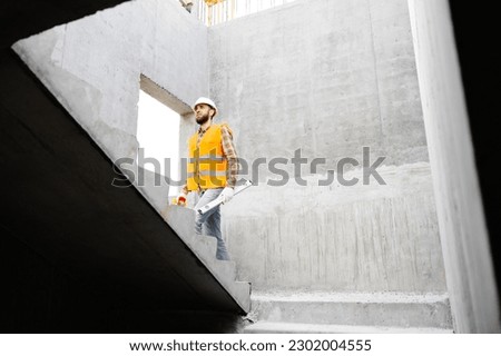 Builder-renovator, foreman in a protective helmet and vest climbs the stairs of the house under construction.