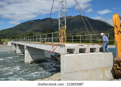 Builders construct a concrete bridge over a small river in Westland, New Zealand