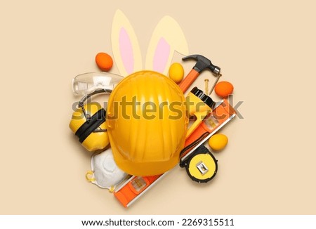 Builder's equipment with bunny ears and Easter eggs on beige background
