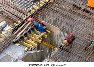 Builders in orange helmets make a steel reinforcement cage for pouring a concrete slab. Steel rods and metal formwork on a construction site. Monolithic construction. Cast-in-place concrete - Shutterstock ID 2156862669