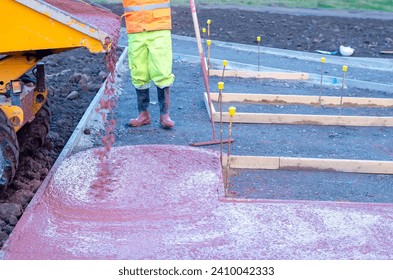 Builders pouring and leveling wet ready-mix concrete into formwork   during new footpath construction