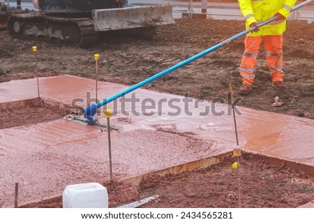 Builders pouring and leveling wet ready-mix concrete into formwork   during new footpath construction