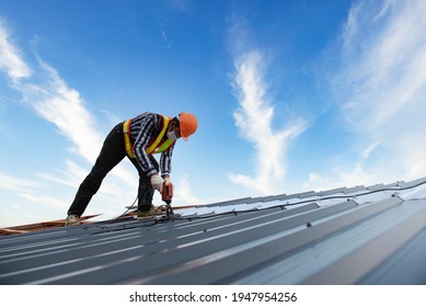 Builders in work clothes install new roofing tools, roofing tools, electric drill and use them on new wooden roofs with metal sheets
