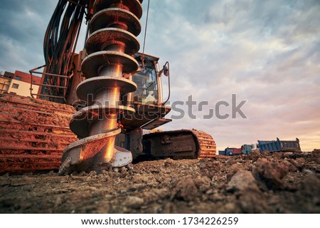 Building activity on contruction site. Close-up view of drilling machine against trucks.  