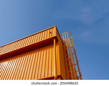 The building is constructed with metal sheet material. painted in yellow throughout with a background of a blue sky during the day.