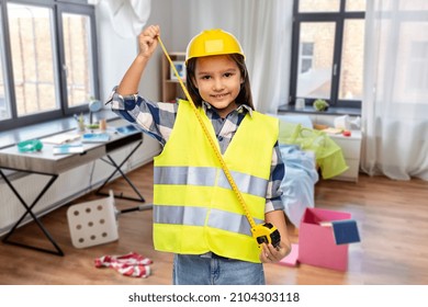 Building, Construction And Profession Concept - Smiling Little Girl In Protective Helmet And Safety Vest With Ruler Over Messy Living Room Background