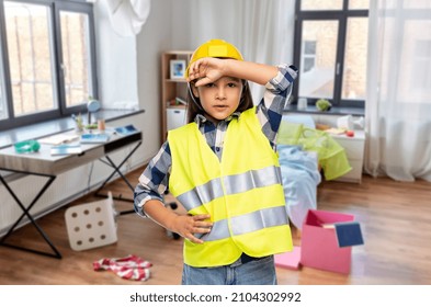 Building, Construction And Profession Concept - Tired Little Girl In Protective Helmet And Safety Vest Over Messy Living Room Background