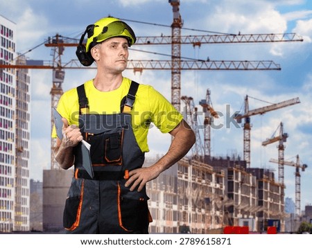 Building construction, site supervision. Construction worker with clipboard inspects high-rise project with tower cranes.