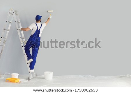 Building contractor painting grey wall with roller brush, copy space text. Construction worker renovating house