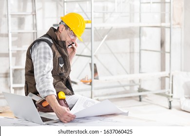 Building contractor talking on a mobile phone as he sits holding a blueprint on a workbench in a room under construction - Powered by Shutterstock