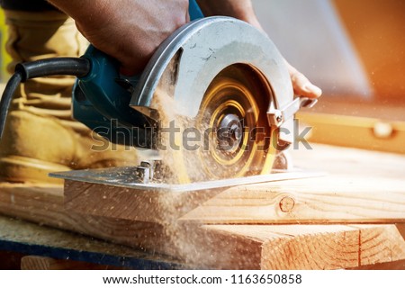 Building contractor worker using hand held worm drive circular saw to cut boards on a new home constructiion project