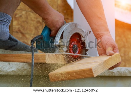 Building contractor worker using hand held worm drive circular saw to cut boards on a new home constructiion project