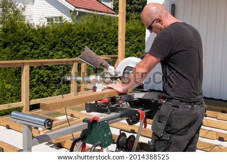 Building contractor worker using hand held worm drive circular saw to cut boards on a new home constructiion project