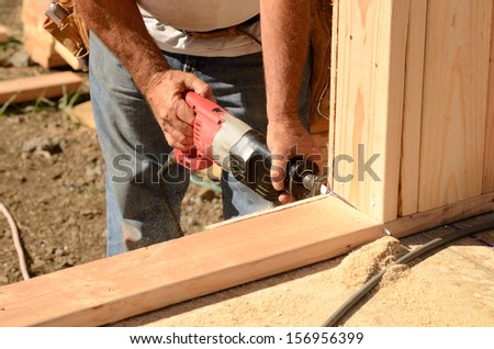 Building contractor worker using a reciprocating saw to cut out the door in the base plate of the wall for the first floor on a new home construction project