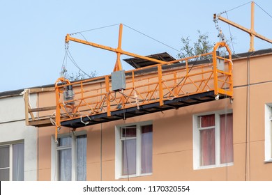 building cradle on the wall of old house on the top floor without workers against the sky. repair of facade of the building. cascading elevator.