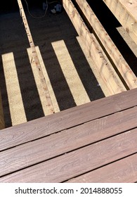 Building A Deck In A Suburban Backyard. The Weathered Wood Foundation Is In Place And The Contractor Is Laying Down Composite Wood And Is Halfway Through The Deck. The Railings Are Demolished.