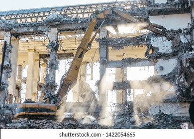 Building Demolition Excavator With Long Mechanical Arm. Destruction Of A House, Reconstruction, Bricks And Metal, Ruins, Concrete Dust In The Air. Heavy Machinery, Hydraulic Construction Equipment.