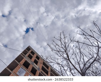 A building with a lot of empty space and a tree in front of it. The sky is cloudy and the sun is shining through the clouds
