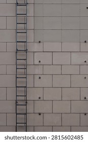 Building facade featuring beige rectangular cladding panels, exposed bolts, and a dark metal fire escape ladder.
