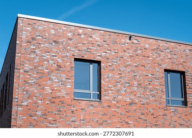 Building facade featuring multicolored red bricks and modern windows under a clear blue sky