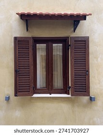 Building facade featuring an old window with brown shutters and a small awning