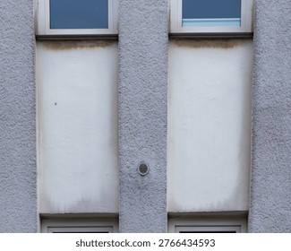 Building facade featuring rough texture, two windows, and water stains from pollution