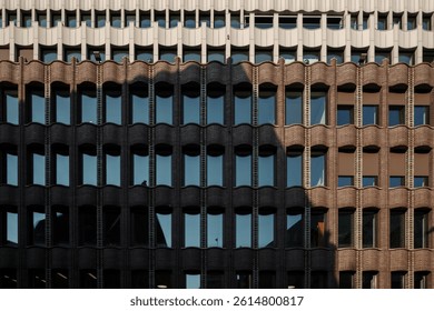 A building facade showcasing a rhythmic pattern of arched brick window frames, transitioning to lighter concrete material at the top. 