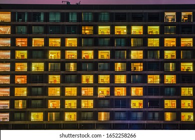 Building Facade Shows A Windows And Rooms Pattern At Night. The Exterior Features Illuminated And Dark Living Spaces With People Living Like Neighbours In A Shared Communal Space. Copenhagen, Denmark