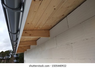 Building fasade under construction with unfinished wall and wooden roof boards with plastic gutter pipes. - Shutterstock ID 1505440922