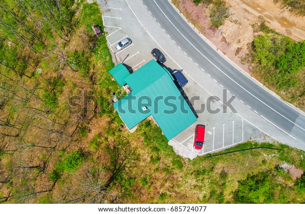 Building with a green roof and parked\
cars on the edge of the road in the forest, top\
view