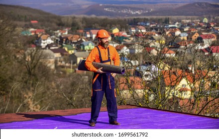 Building House. Apply Plastic Coatings Membranes Fiberglass Or Felt Over Sloped Roofs Before Applying Shingles. Roofer Repair Roof. Roof Installation. Man Hard Hat Work Outdoor Landscape Background.