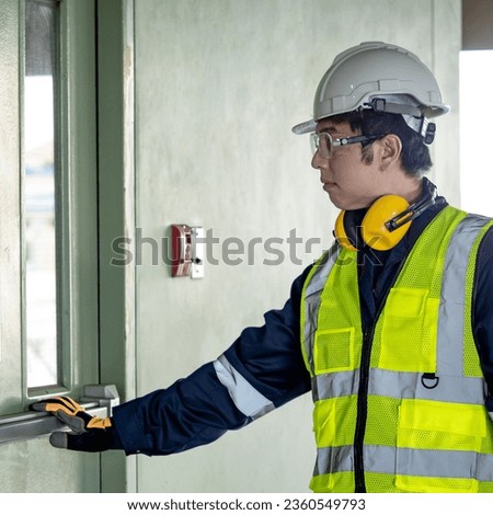 Building inspector man pushing panic bar or crash bar on fire exit door. Asian male construction worker with reflective vest, safety helmet and goggles checking door hardware for safety and security